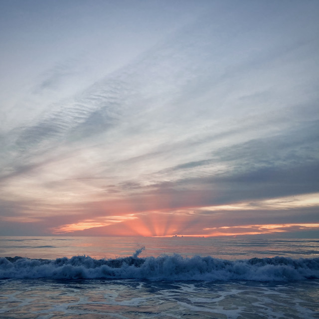 The sun begins to rise over the ocean. A small wave is coming up over the surf.