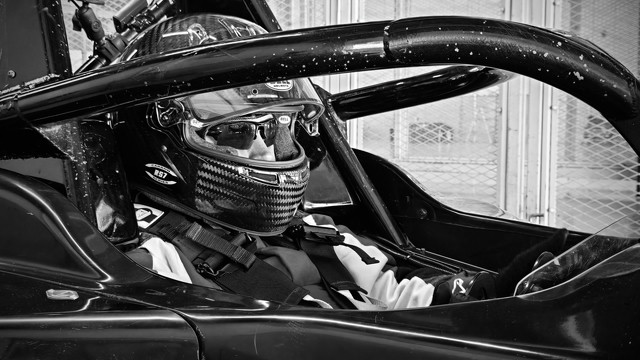 Me sitting in a race car cockpit. My visor on my helmet is up as I do final checks.