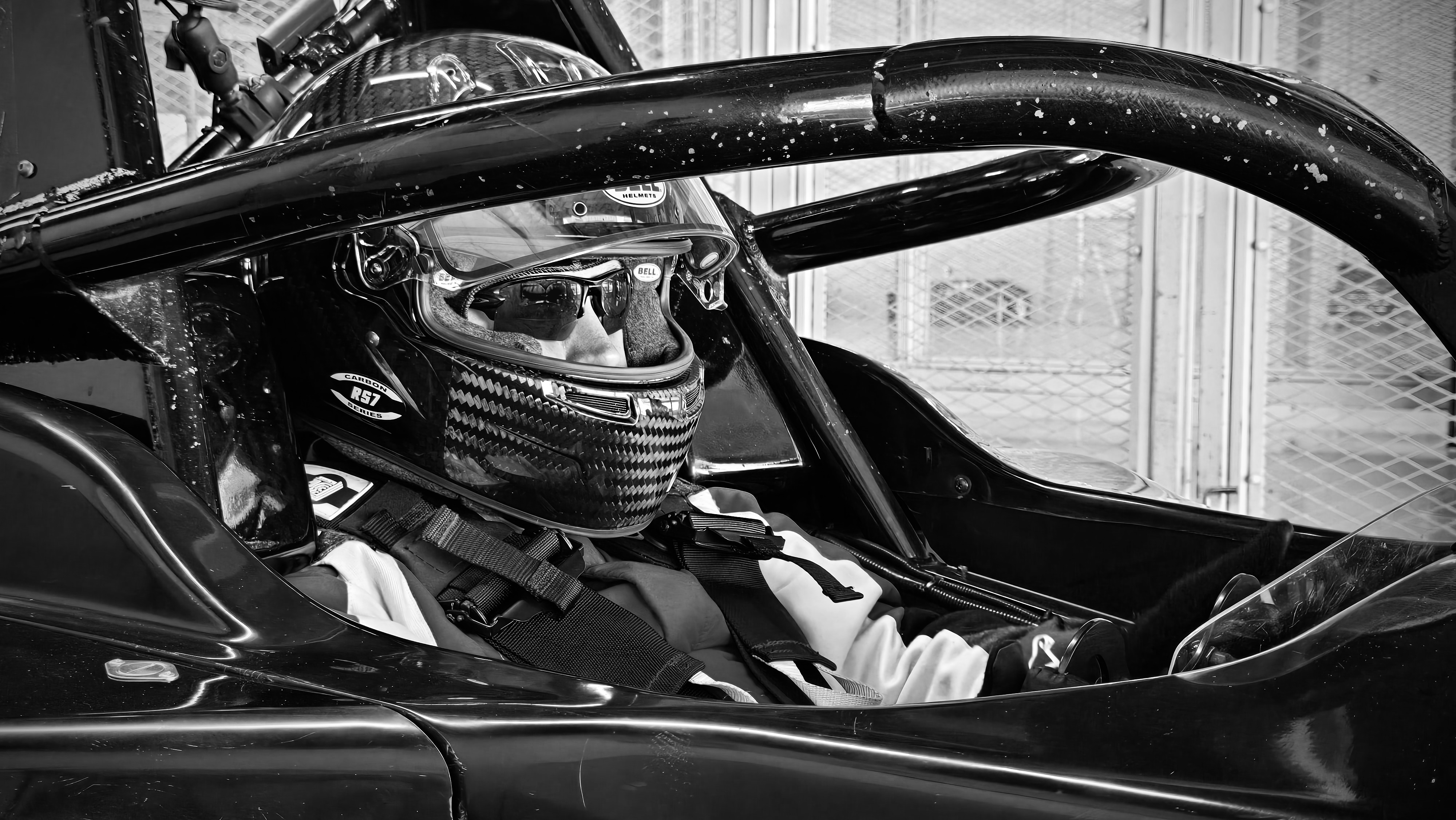 Me sitting in a race car cockpit. My visor on my helmet is up as I do final checks.