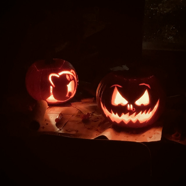 Two carved lit up pumpkins. One has a Kirby design, the other is a classic grinning jack o lantern.