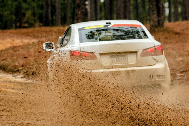 A white Lexus IS250 slides through a turn, kicking up an insane amount of mud at the camera in the process.