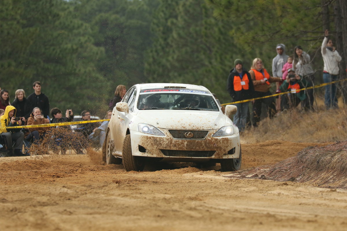 A white Lexus IS250 slides through a turn. Spectactors can be seen in the background.