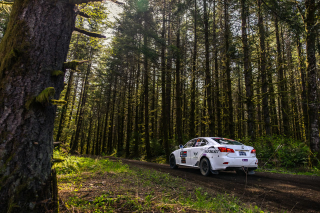 A white Lexus IS250 rally car racing through the woods.