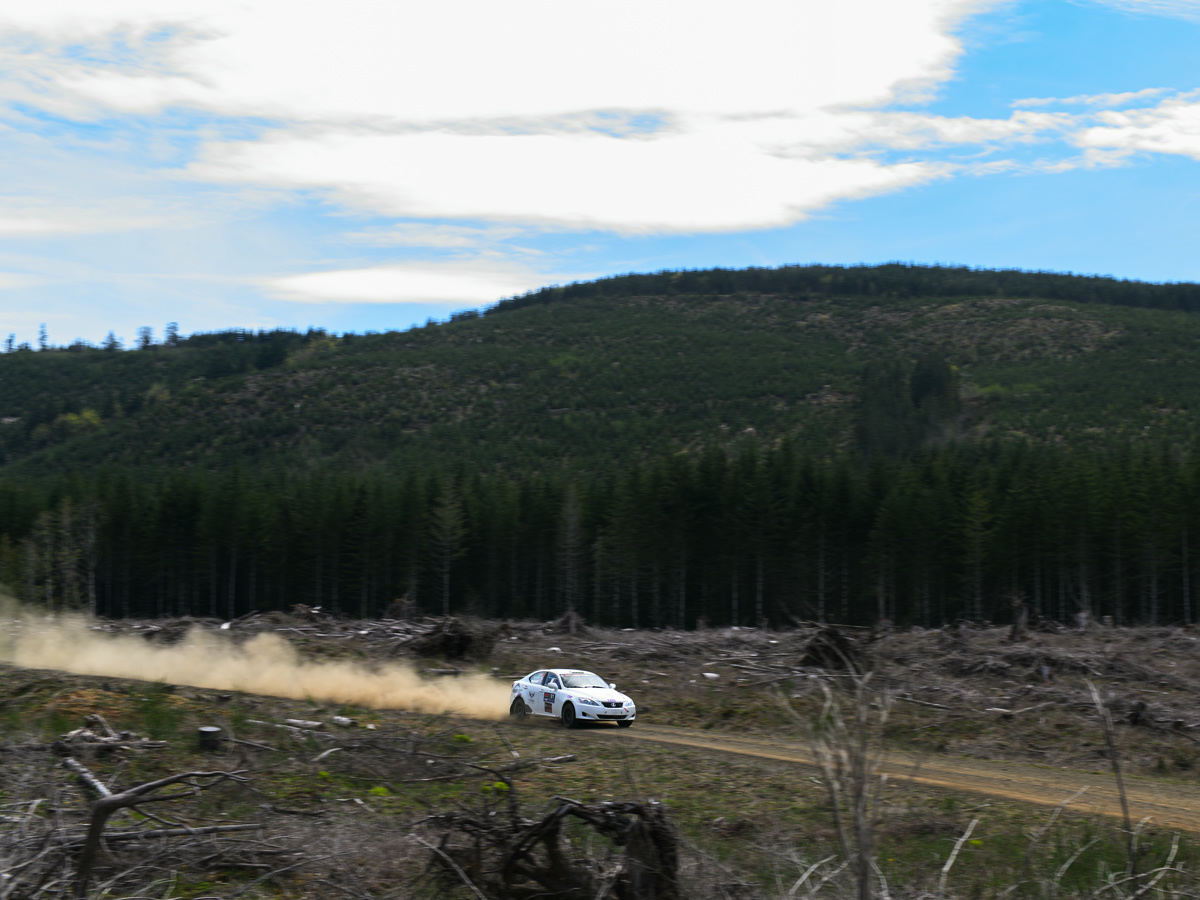 A white Lexus IS250 booking it down a closed off logging road. A large dust cloud can be seen behind it.