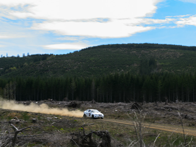A white Lexus IS250 booking it down a closed off logging road. A large dust cloud can be seen behind it.