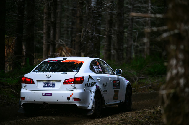 A white Lexus IS250 sits in a deep green forest, ready to start a stage.