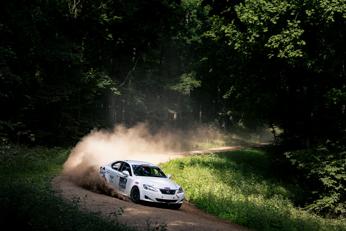 A white Lexus IS250 powers through a turn. Massive dust clouds can be seen behind it.