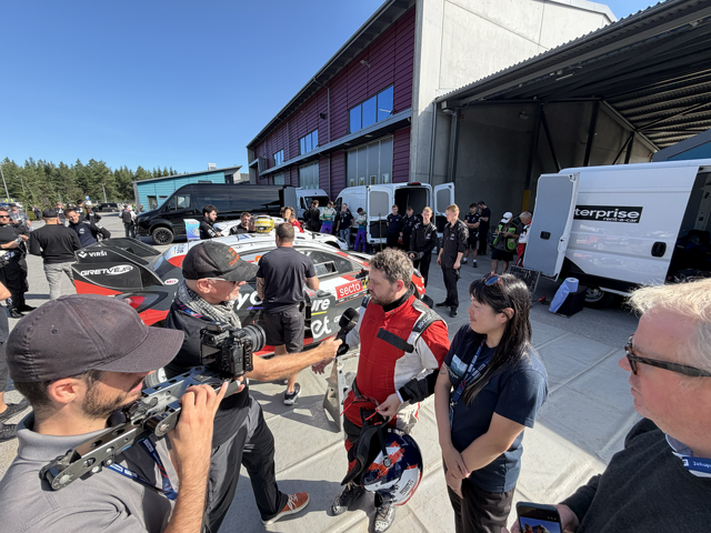 Me in a racecar service park being interviewed. Many people are around the car working on getting it back out for the next run.