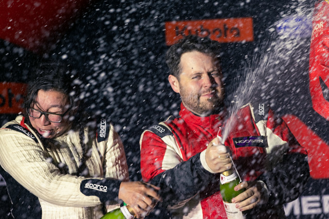 My co-driver in a white suit and me in a red suit spraying champagne on the podiums.