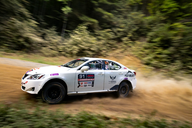 A close up of a white Lexus IS250 sliding mid-turn in the woods.