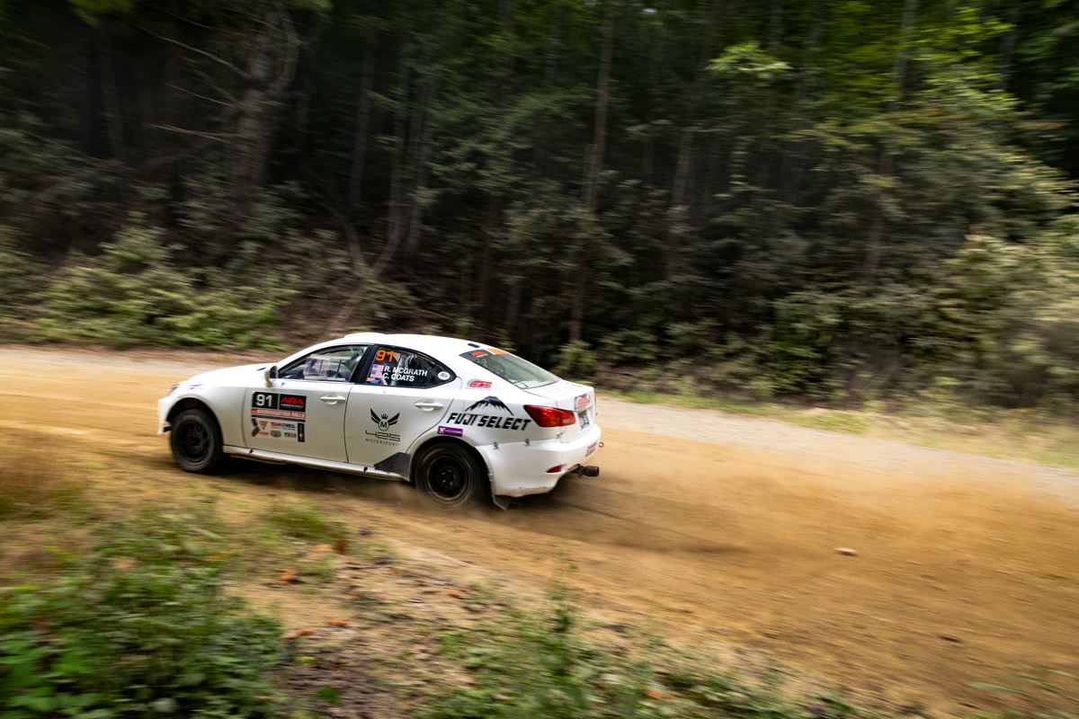 A white Lexus IS250 exiting a turn in the woods at speed.