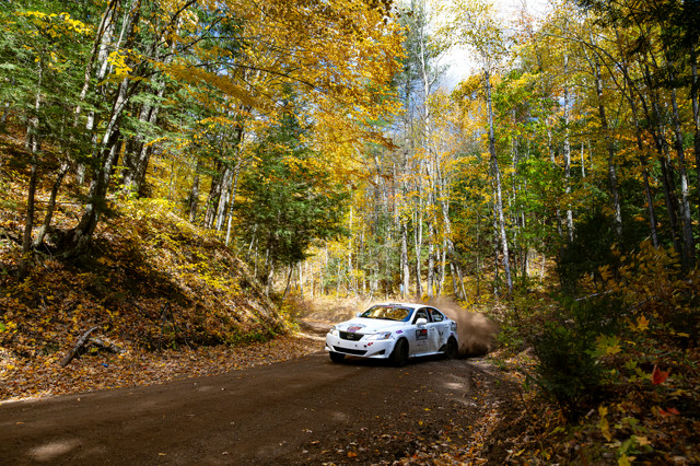 A white Lexus IS250 slides through a turn in a forest draped in warm autumn colors.